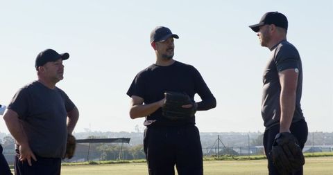 Baseball teammates discussing strategy on sunny field wearing caps and mitts