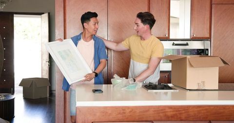 Diverse male couple unpacking in modern kitchen with artwork