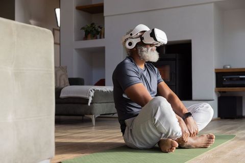 Senior african american man using vr headset for guided meditation and relaxation on home yoga mat