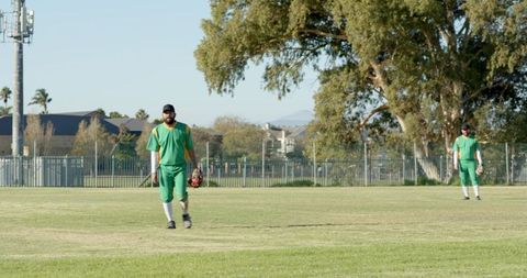 Outfield Teammates Walking and Standing in Green Baseball Uniforms on Suburban Field