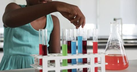 Young student mixing colorful test tubes conducting hands-on science experiment in school laboratory