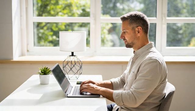 Mature man working on laptop in bright minimalist home office by window