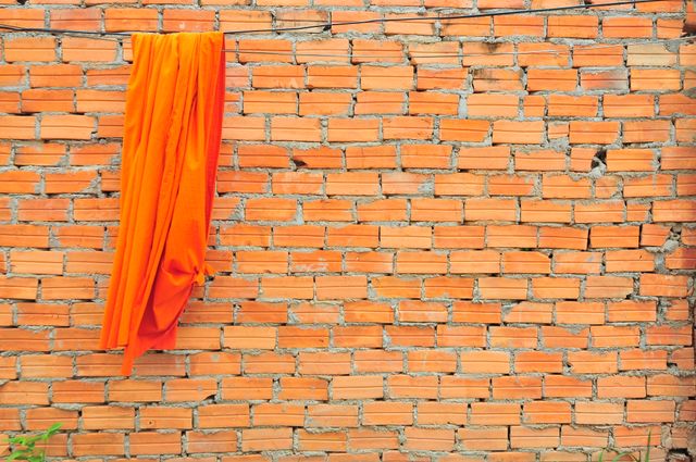 This image depicts vibrant orange fabric draped over a rustic brick wall, creating a strong contrast between the soft, colorful textile and the rough, urban brick surface. Suitable for design projects emphasizing color contrast, urban settings, or rustic textures. Perfect for creative backgrounds, architectural presentations, or advertising campaigns focusing on vibrant, eye-catching visuals.