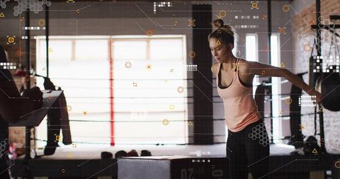 Woman balancing on plyo box in warehouse gym during plyometric workout with hud graphics