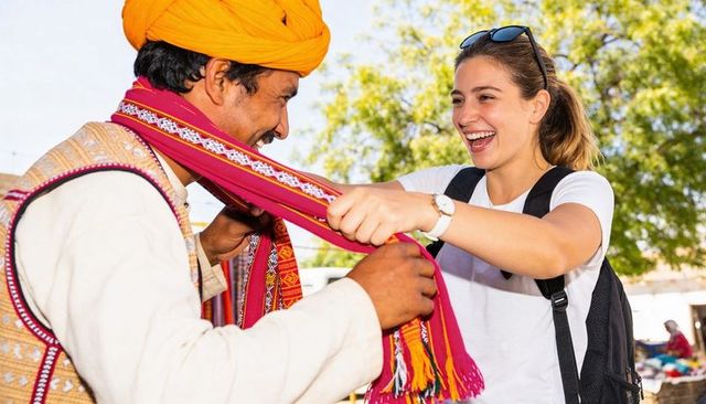 Tourist laughing while trying vibrant handwoven scarf from smiling local vendor