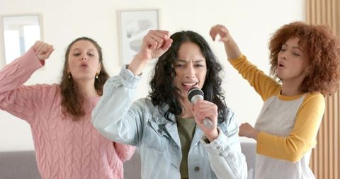 Diverse friends singing together during home karaoke holding microphone and cheering