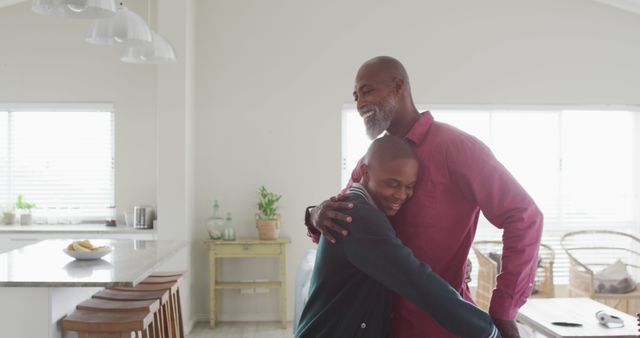Father and son sharing an affectionate hug in a bright, modern kitchen. The photo depicts family bonding and domestic happiness. The setting can be a useful representation for themes such as family, love, relationships, and everyday life. Ideal for advertisements, websites, parenting blogs, and articles focused on family values and home living.