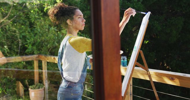 Biracial woman painting on canvas in the balcony at home. staying at home in self isolation in quarantine lockdown