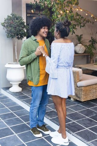 Holding hands and smiling: diverse young couple embracing on cozy courtyard patio at dusk