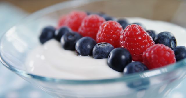 A bowl of yogurt topped with fresh blueberries and raspberries offers a healthy snack option, with copy space. Vibrant berries add a pop of color and nutritional value to the creamy yogurt.