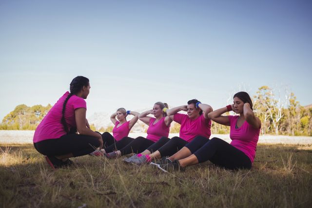 Group of women participating in an outdoor boot camp with a female trainer. They are performing exercises on a grassy field under a clear sky. Ideal for promoting fitness classes, outdoor activities, group workouts, and healthy living.