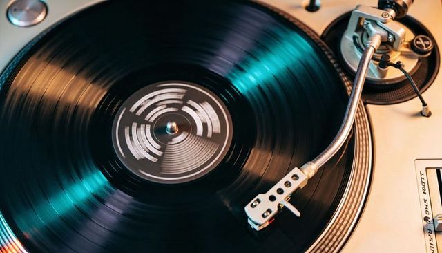 Spinning vinyl record on vintage turntable with chrome tonearm and teal reflections
