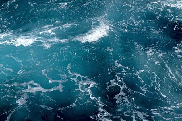 This image features an aerial view of deep turquoise ocean waves crashing against each other, showcasing the natural beauty and turbulence of the sea. Ideal for use in environmental campaigns, travel brochures, background wallpapers, and maritime industry marketing.