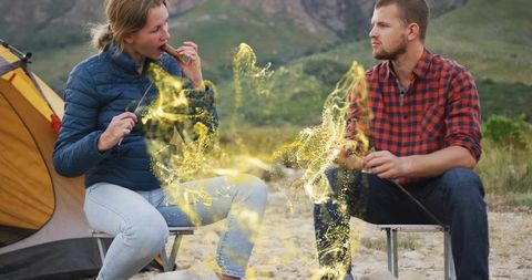 Couple roasting skewers at mountain campsite with golden ember glow and cozy tent vibe