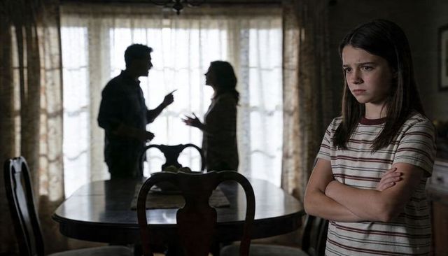 Teen standing with arms crossed while parents arguing in backlit dining room silhouette
