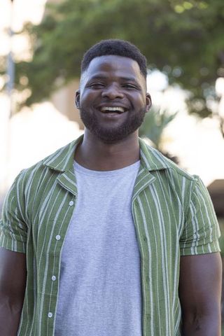 Smiling african american man standing outdoors wearing green striped shirt and gray tee