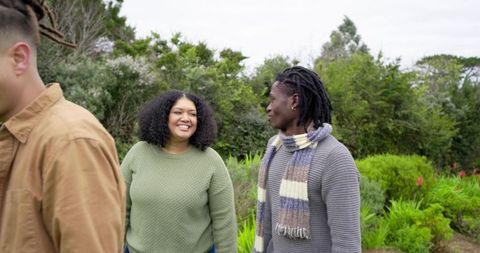 Diverse friends walking and chatting in garden, casual knitwear and autumn scarf