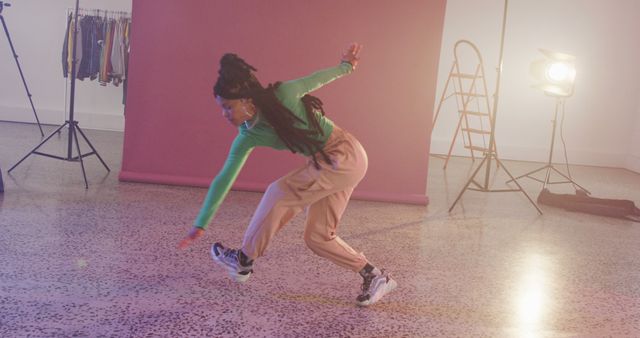 Young woman performing breakdance move in studio against pink backdrop, showcasing urban dance culture and street style. Suitable for using in promotions for dance schools, urban fashion, and energetic lifestyle.