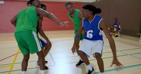 Competitive indoor basketball players driving, dribbling and defending on gym hardwood