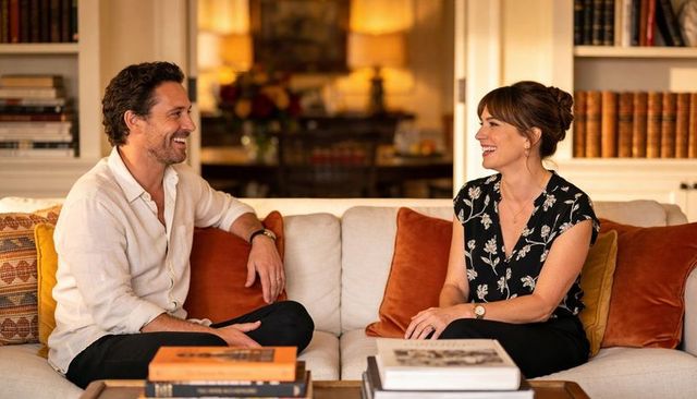 Smiling couple chatting on cozy sofa with books, warm lamps and rustic decor