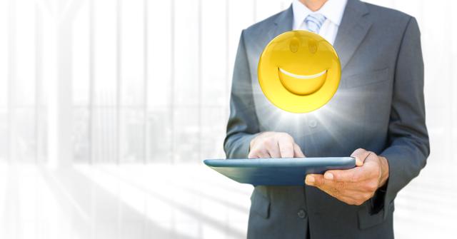 Image depicts businessman using tablet with overlay of smiling emoji and light flare effect. Useful for business, technology, and communication concepts. Great for projects highlighting modern digital interaction and professional environments.