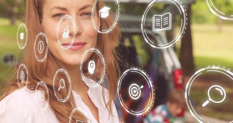 Woman standing in park with augmented reality education icons overlaying pickup and child