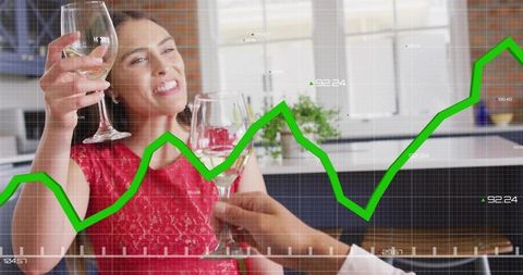 Couple toasting with wine in modern kitchen while green stock market graph rises