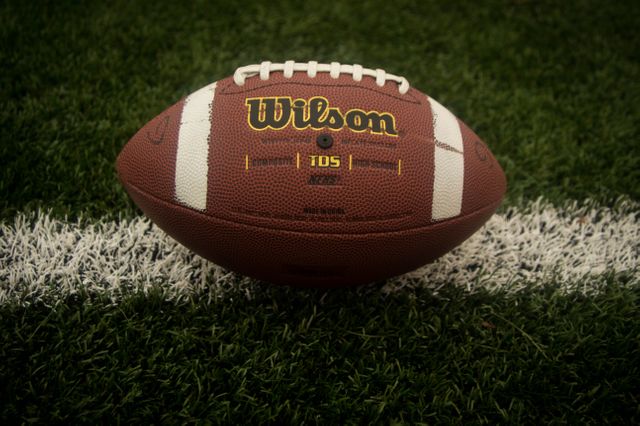 High-quality image of a Wilson football lying on a grass field, perfect for use in sports-related articles, websites, or advertisements. Great visual for illustrating concepts related to football, team sports, and athletic equipment.