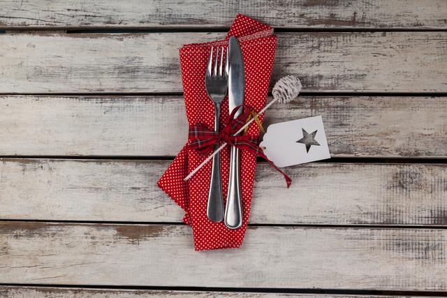 Cutlery tied with a red polka dot napkin and a star tag on a rustic wooden table. Ideal for use in holiday dining themes, restaurant promotions, or country-style home decor.
