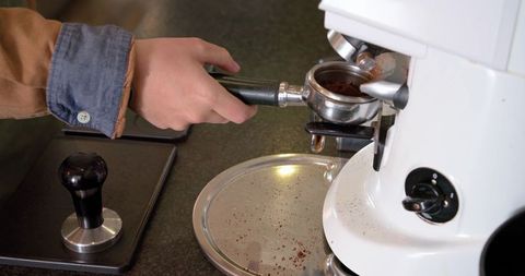 Woman barista preparing espresso with portafilter and grinder over stainless drip tray