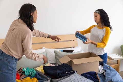 Mother and white teenage daughter packing and sorting clothes in bright cozy bedroom