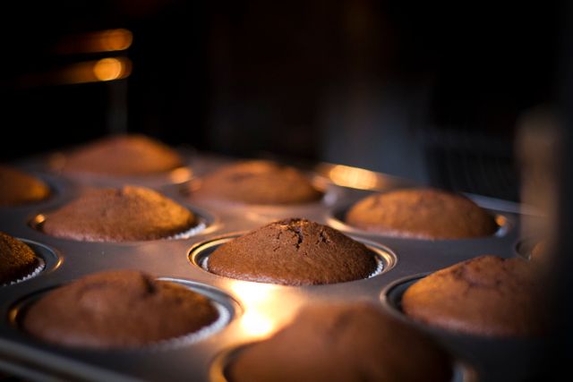 Close-up view of freshly baked chocolate muffins in baking tray inside oven. Warm lighting enhances the cozy feel of freshly made desserts. Perfect for illustrating concepts related to baking, home cooking, desserts, recipes, and food photography.