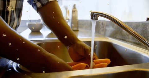 Adjust hands washing carrots under chrome faucet in kitchen