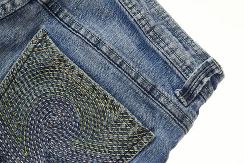 Showcasing embroidered spiral pocket detail on vintage blue denim jeans with belt loop