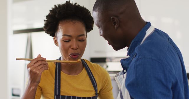 This image showing a happy African American couple cooking together can be used in various scenarios to illustrate themes of love, togetherness, and quality time at home. It is perfect for advertisements and promotions related to cookware, cooking classes, and culinary products. It can also be featured in lifestyle blogs, relationship counseling materials, and content focusing on family values, nutrition, and wellness.