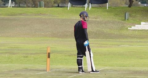Cricketer Ready to Bat on Field with Equipment and Stumps in View