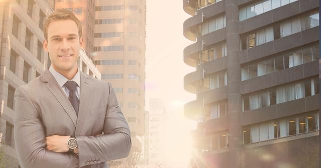 Young businessman with a confident expression standing with arms crossed against the backdrop of modern city buildings during sunset with a sun flare. Perfect for business-related themes, corporate presentations, and professional portfolios.