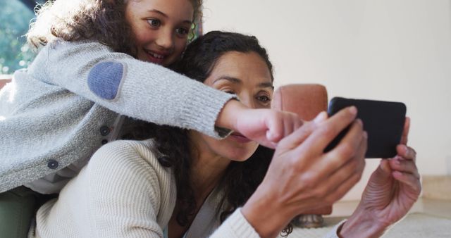 Mother smiling with daughter while taking a selfie; perfect for family, parenting, and togetherness themes.