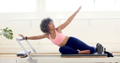 Curly-Haired Woman Practicing Pilates on Reformer Machine - Download Free Stock Images Pikwizard.com