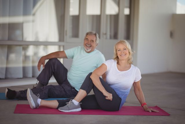 Senior couple performing stretching exercises on yoga mats at home. They are smiling and appear to be enjoying their workout. This image can be used for promoting healthy lifestyles among seniors, fitness programs for the elderly, or wellness and retirement living.