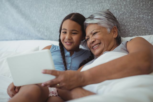 Grandmother and granddaughter using digital tablet in bed room at home