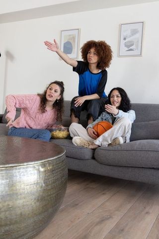 Diverse friends cheering on couch with snacks and basketball during lively game night