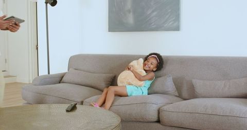 Young Girl Hugging Teddy Bear on Couch in Modern Living Room