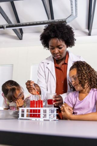 African-american scientist teaching children pipetting bright red solution in school lab