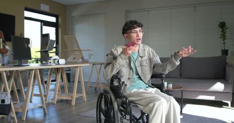 Young man in wheelchair speaking on smartphone and gesturing in creative studio office