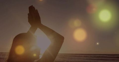Woman practicing yoga on beach at sunset with golden sun flare and meditative silhouette