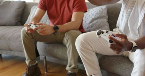 Multiracial friends playing video games on couch, casual home gaming with controllers