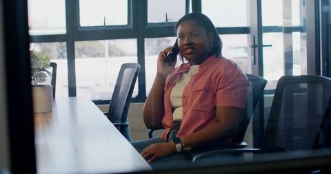 African american woman talking on smartphone in modern office boardroom wearing pink shirt