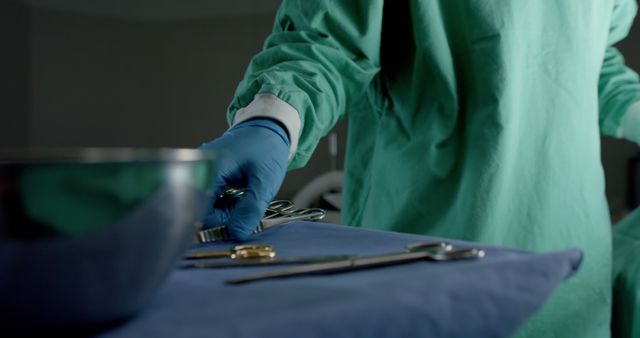 Surgeon in green gown and blue gloves arranging surgical tools on a sterile table. Ideal for use in contexts related to medical procedures, healthcare environments, surgical preparations, hospital settings, and professional healthcare promotion.