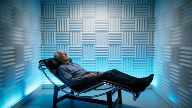Elderly man reclining on chaise in led-lit acoustic foam room for deep relaxation